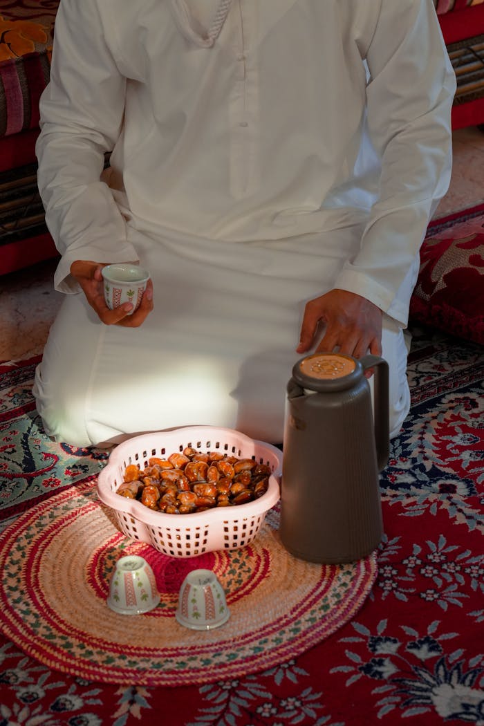 Omani man enjoying a traditional moment with dates and tea on a vibrant patterned rug.